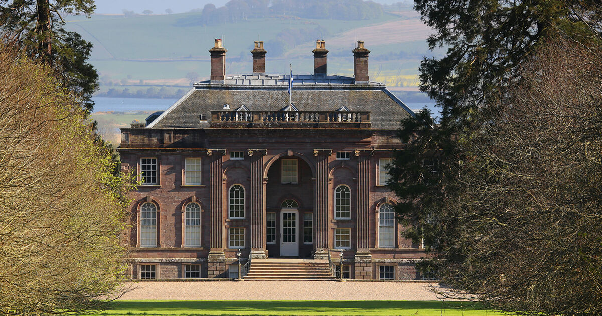 A large, symmetrical Georgian-style mansion with tall chimneys, large windows, and steps leading to the main entrance, surrounded by trees and a manicured lawn with hills in the background.