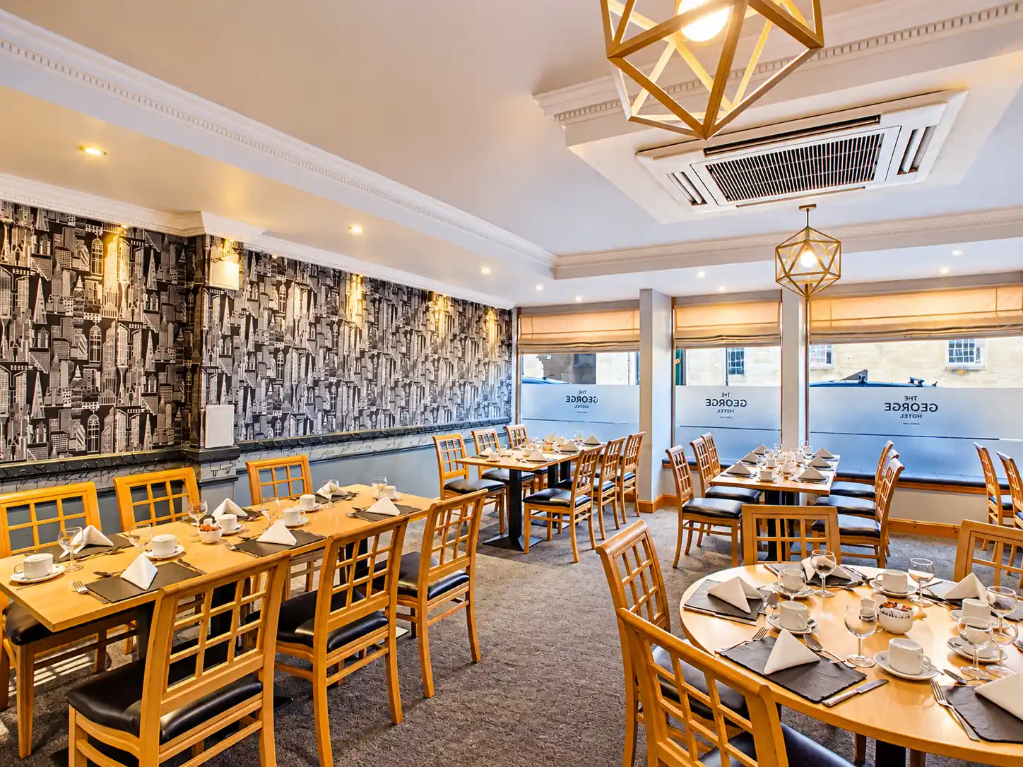 A dining room at The George Hotel with multiple tables set for service, patterned wallpaper, and geometric light fittings.
