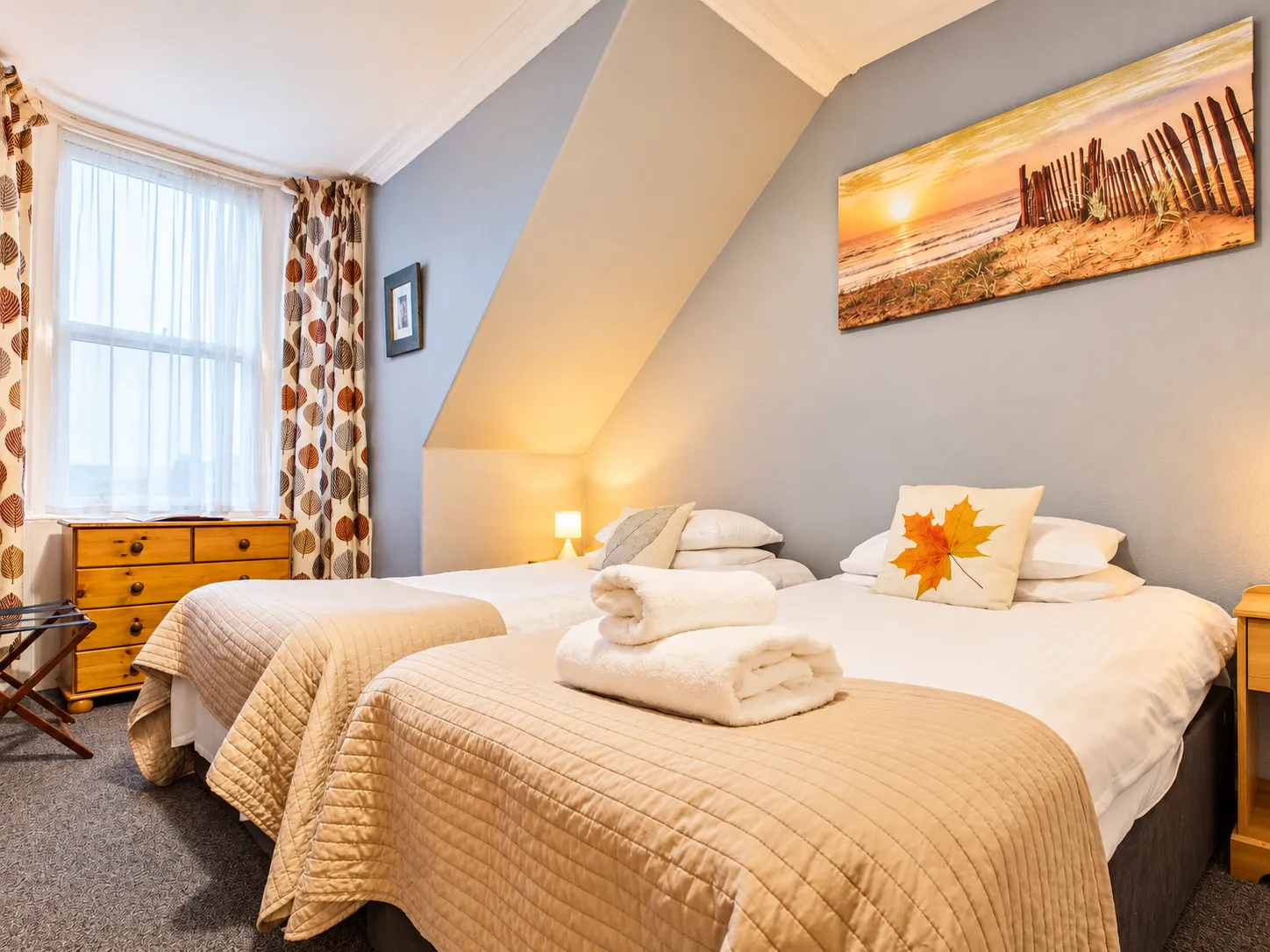 Bedroom with two single beds featuring tan quilted coverlets, a small lamp, and wall art of a sunset beach scene.